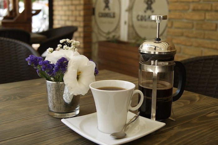 A cup of coffee on a table, with a french press.