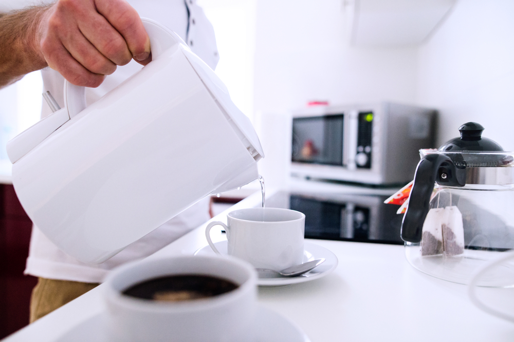 Two white cups of coffee with a hand pouring through awhite pitcher
