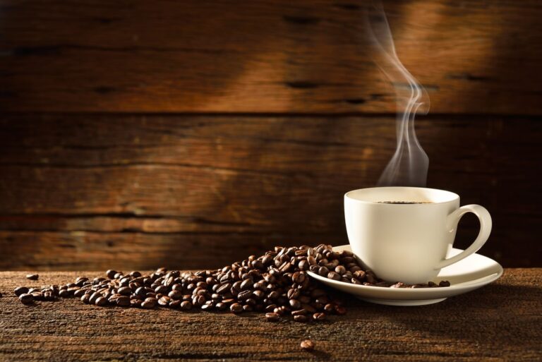A cup of coffee sitting on top of a wooden table with coffee beans.