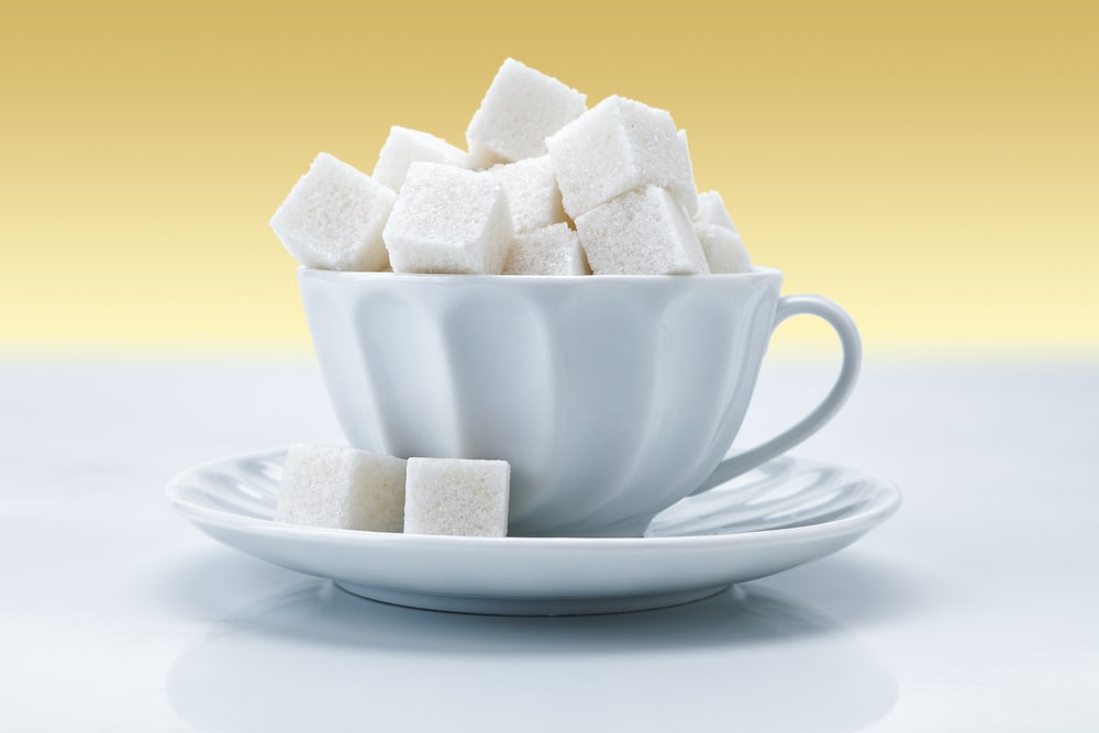 A cup of coffee on a table, with Sugar and Cake