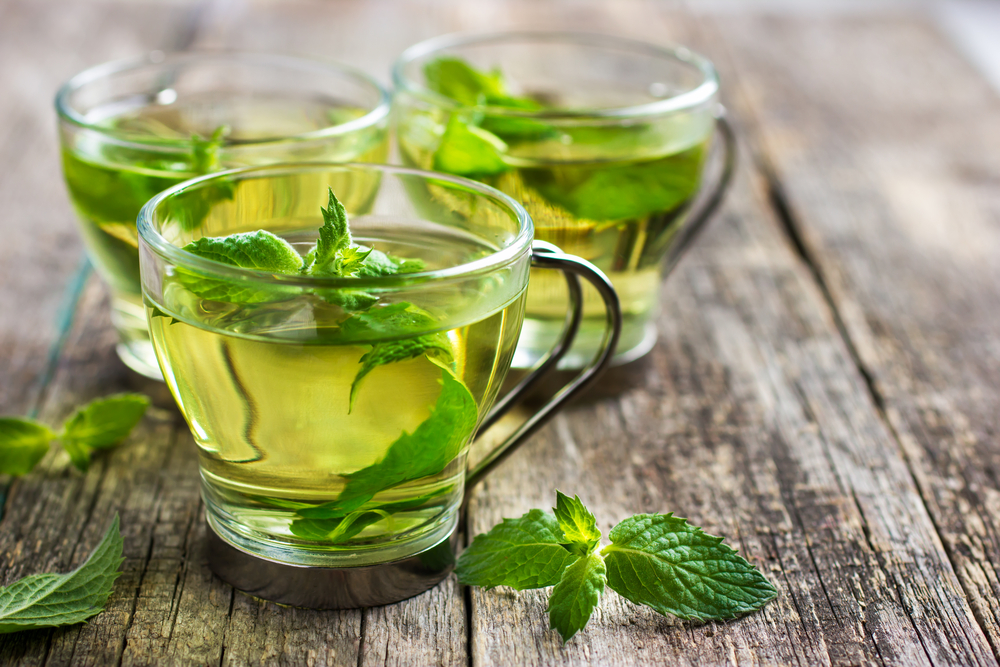 Hot mint tea in glass cup on wooden background, selective focus