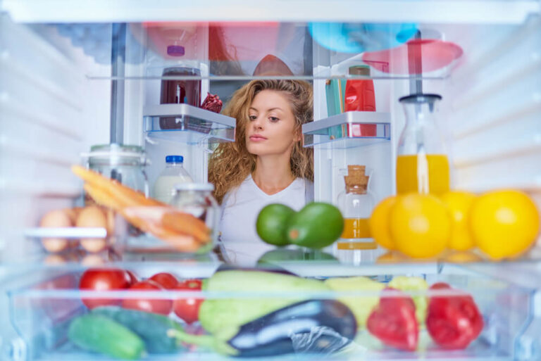 Woman standing in front of fridge full of groceries items and drinks - how long does tea last in the fridge