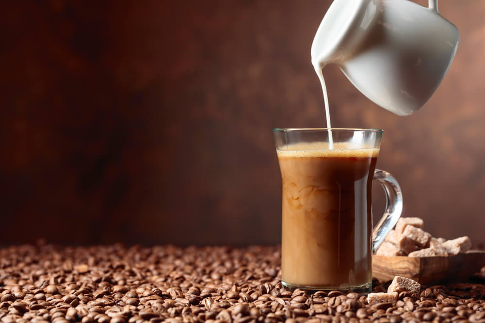 nitro cold brew coffee getting poured by steamed milk and coffee beans scattered