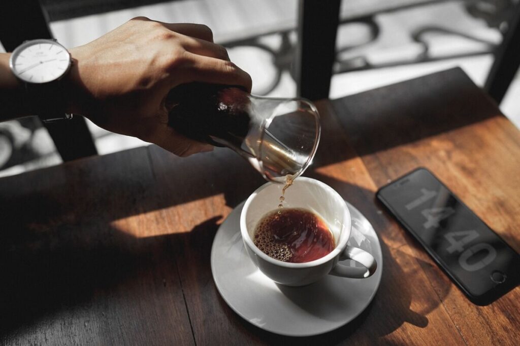a man pouring coffee in his cup with a cellphone beside the cup