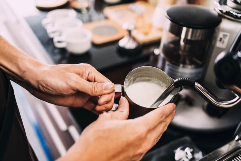 Close-up barista hands frothing warm milk on a coffee machine
