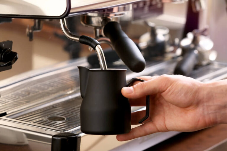 Barista whipping milk using a black frothing pitcher