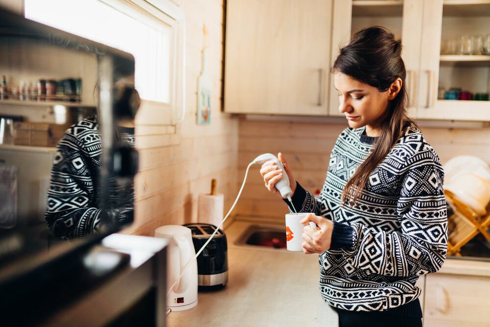 Woman making coffee drink at home kitchen using electric milk frother - will a milk frother mix protein powder