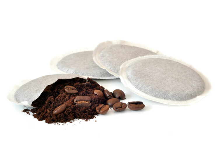 Four white coffee pods with the contents of one pod exposed