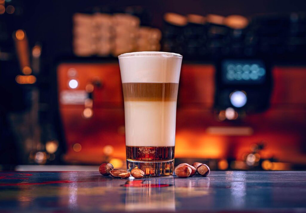 a cup of hot macchiato latte with coffee beans beside it
