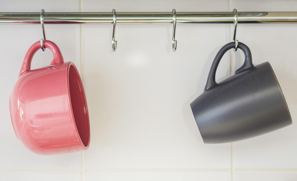 two coffee mugs hanging on a cabinet