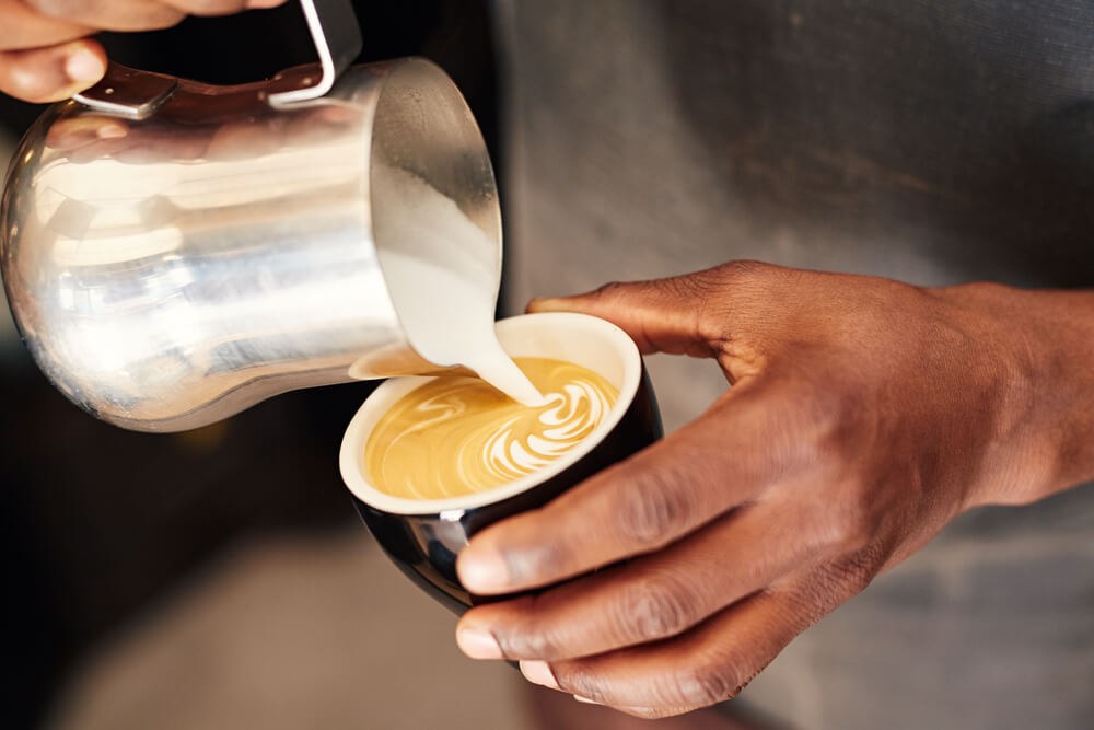 a man holding a cup of latte while pouring down whole milk