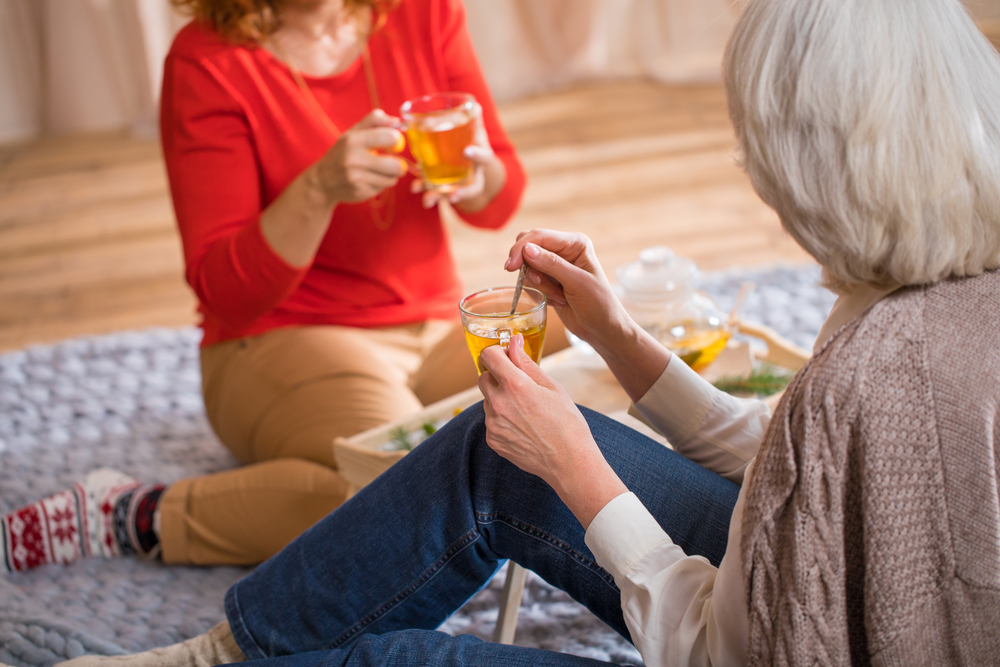 two women casually talking while holding both teas