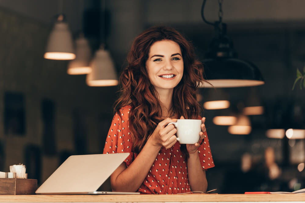 a woman smiling while holding her cup of coffee