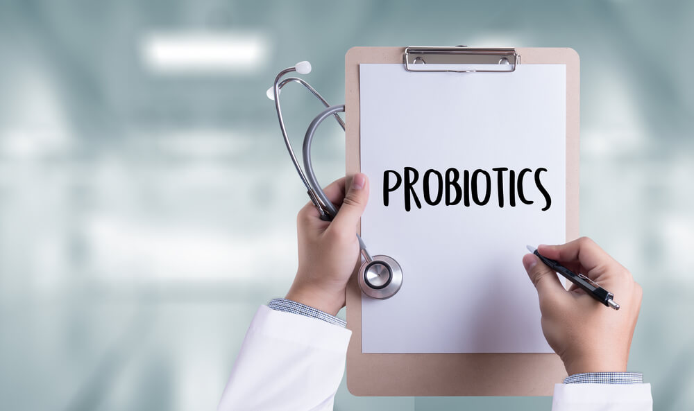 a hand holding a pen and a stethoscope with a pad that has a writing probiotics