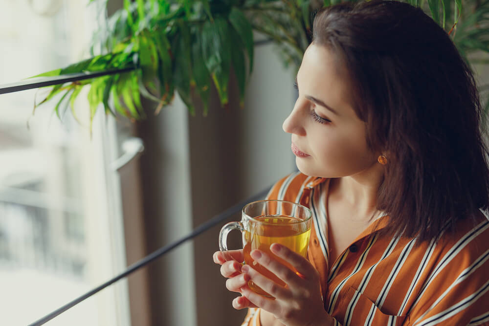 woman looking at the window while holding a tea