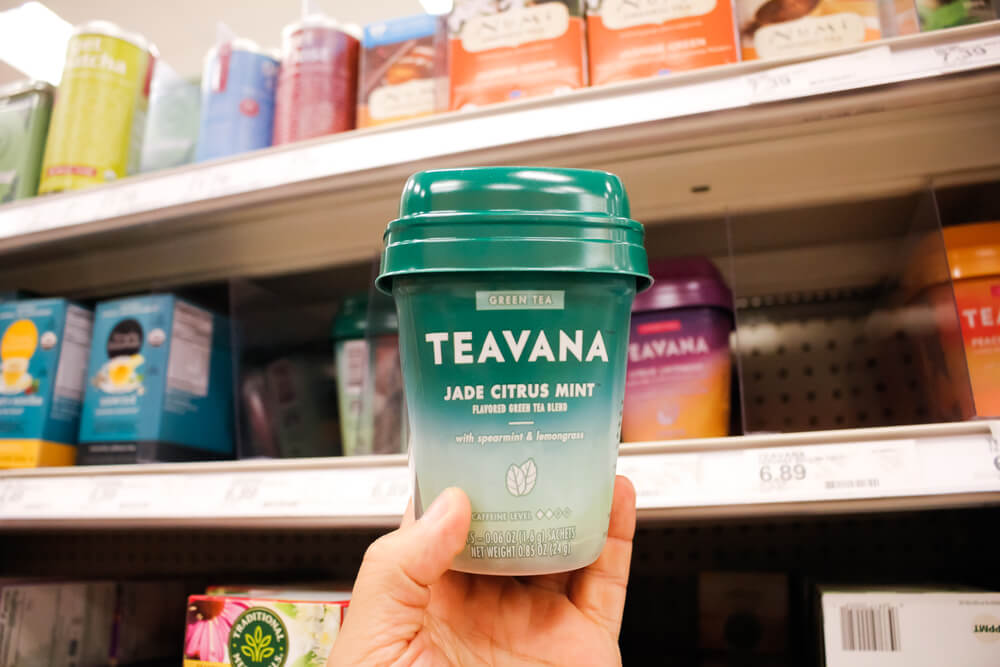 A hand holds a container of Teavana tea sachets