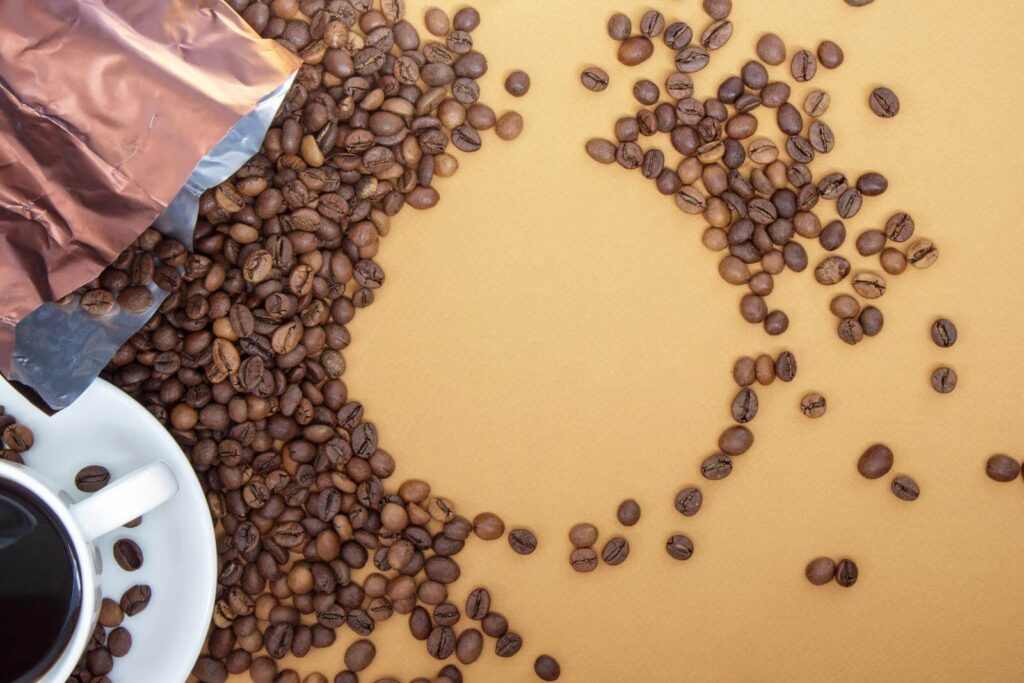 White cup of Americano black coffee without milk with a bunch of roasted coffee beans scattered from packaging