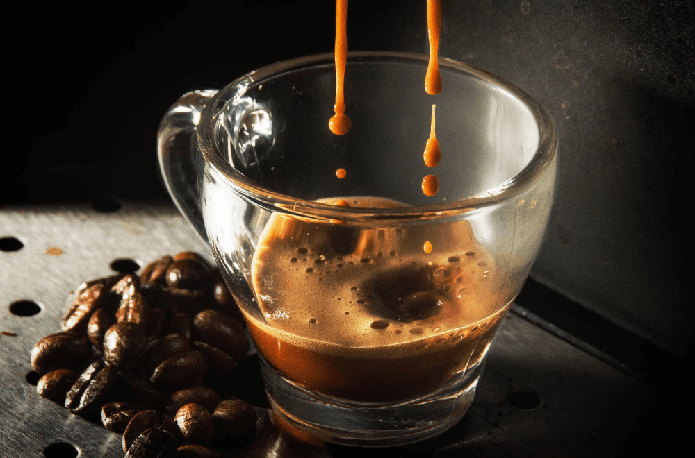 Dripping espresso in a cup with coffee beans beside