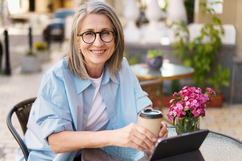 Grey hair charming woman drinking coffee sitting at a table in a street cafe