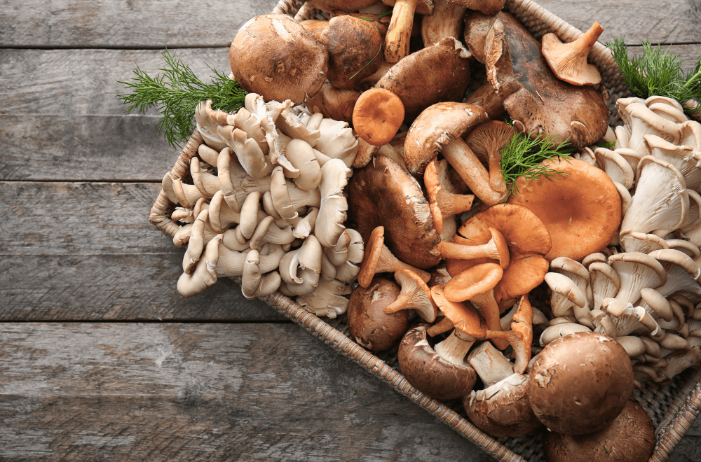 Wicker tray with a variety of raw mushrooms on wooden table