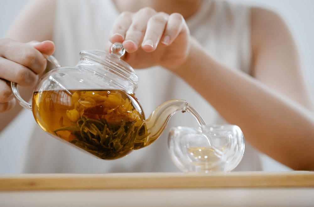 A woman pouring tea from a glass teapot