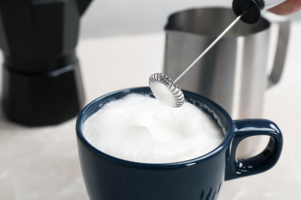 Professional milk frother creating creamy foam for cappuccino and latte drinks