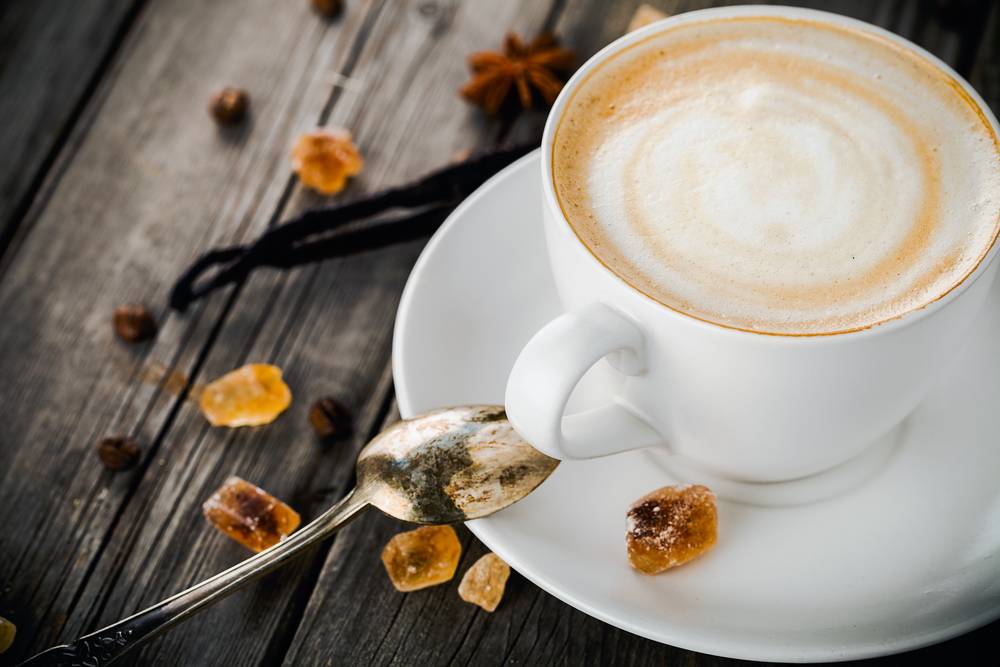 cup of cappuccino, vanilla stcks, anise stars, coffee bans, sugar and old metallic spoon on old wooden table