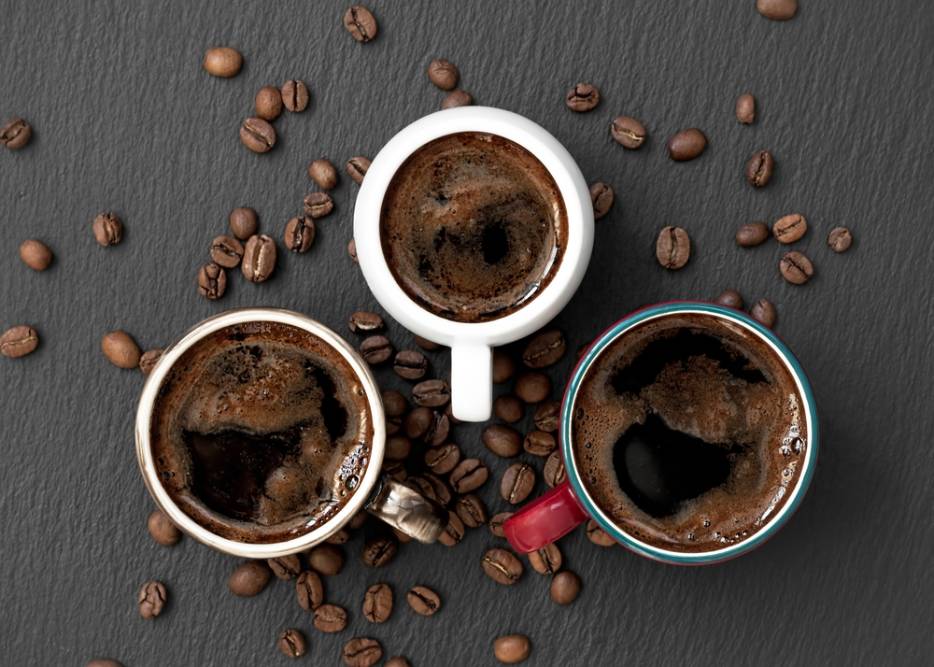 Three multi-colored cups with aromatic espresso coffee on a black stone background