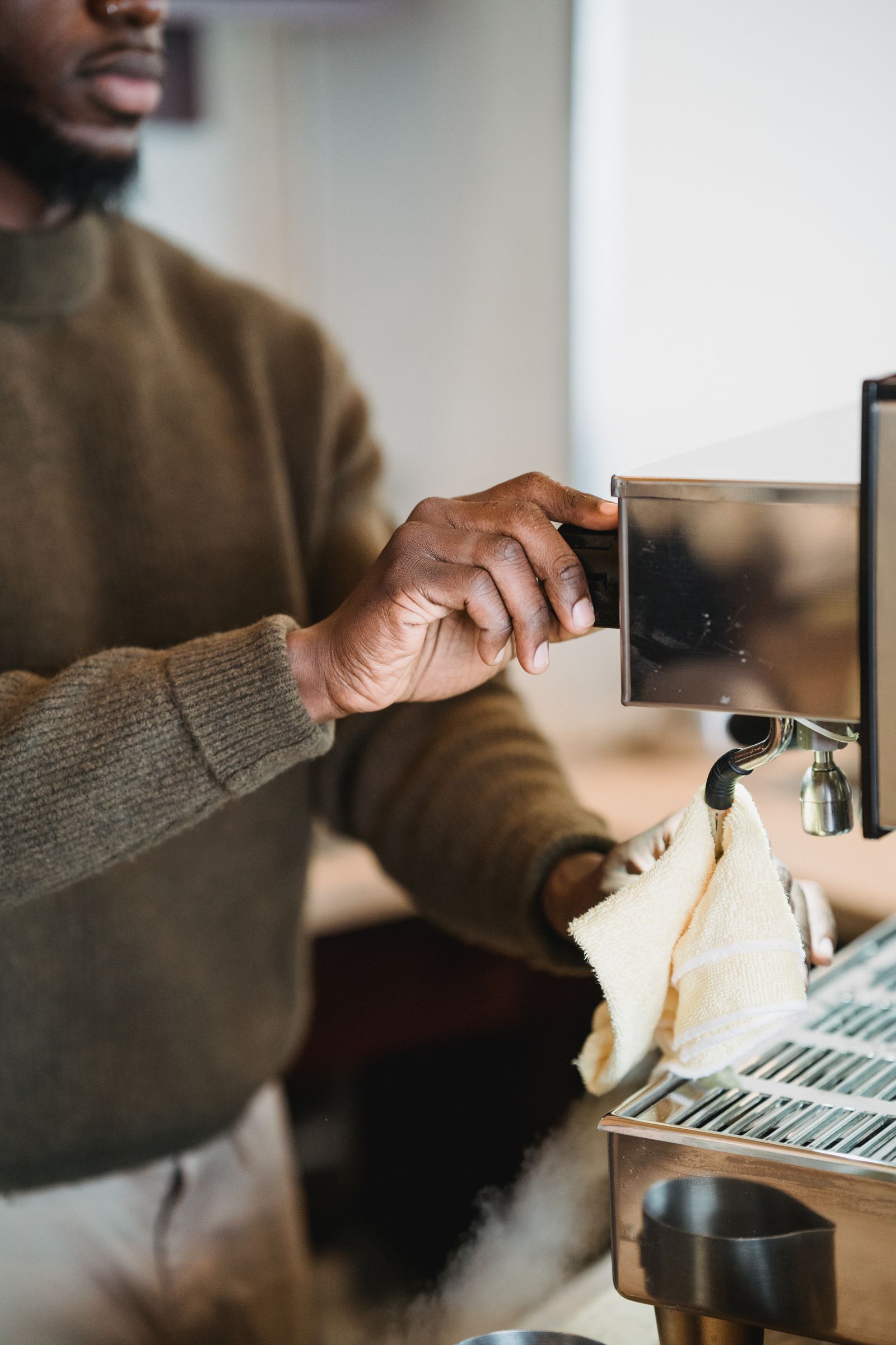 A person wiping a commercial espresso machine with a cloth.