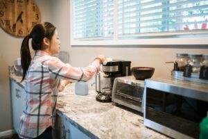 A person wiping a drip coffee maker on a home kitchen counter.