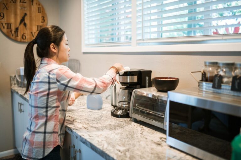 A person wiping a drip coffee maker on a home kitchen counter.