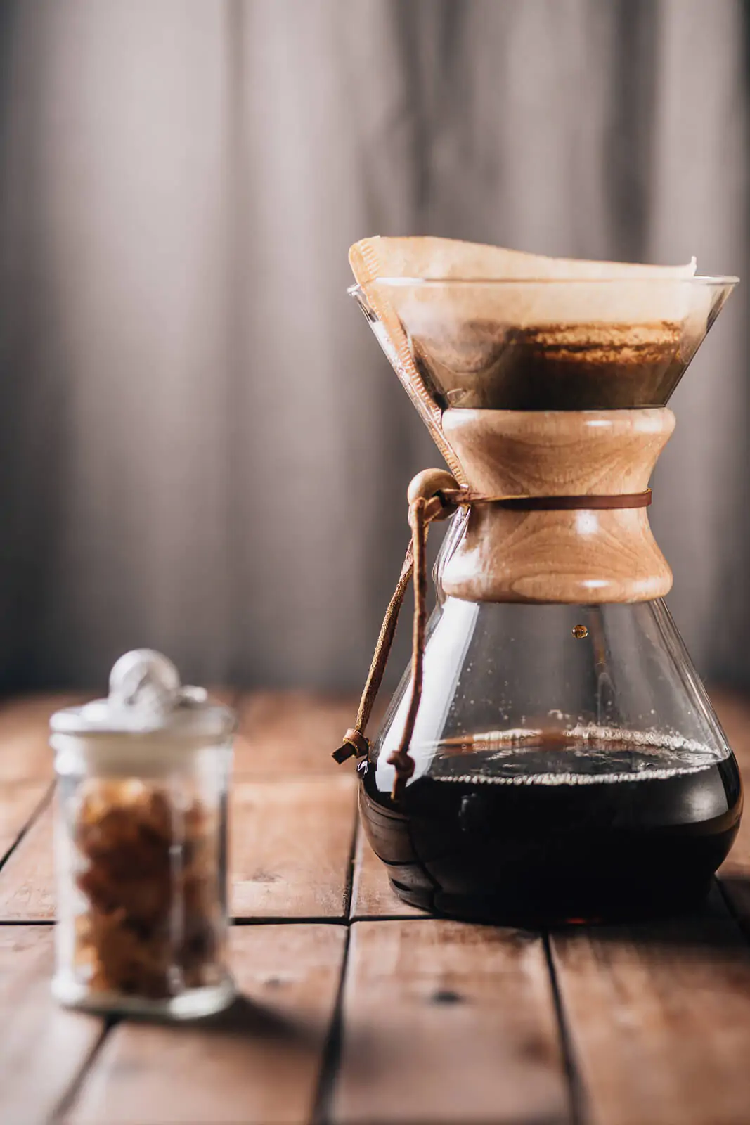 A tabletop scene with coffee running through a coffee maker and some rock candy on a wooden table