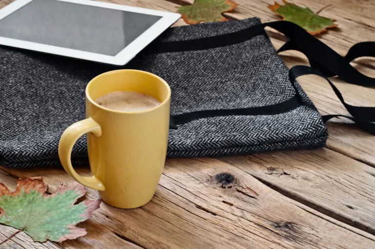 Cup of cappuccino with female woolen bag and tablet