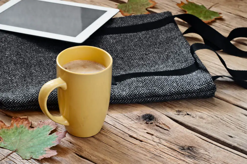 Cup of cappuccino with female woolen bag and tablet