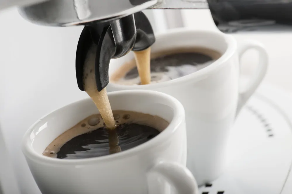 Coffee dripping into two white cups from a coffee machine.