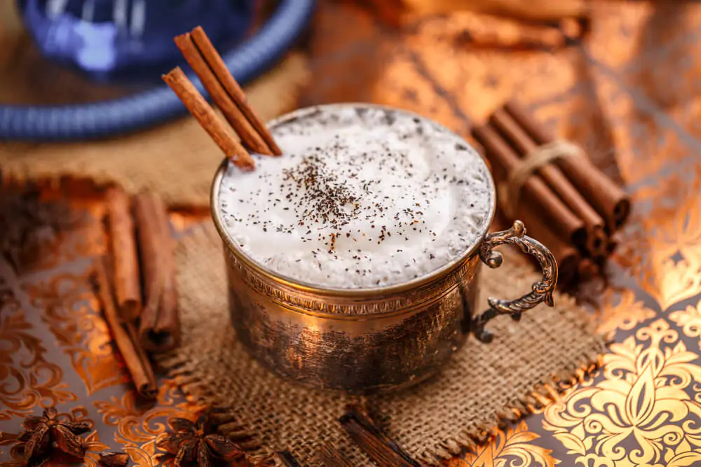 Does chai latte have sugar. A cup of chai latte with three cinnamon rolls in it and some cinnamon rolls on the table.
