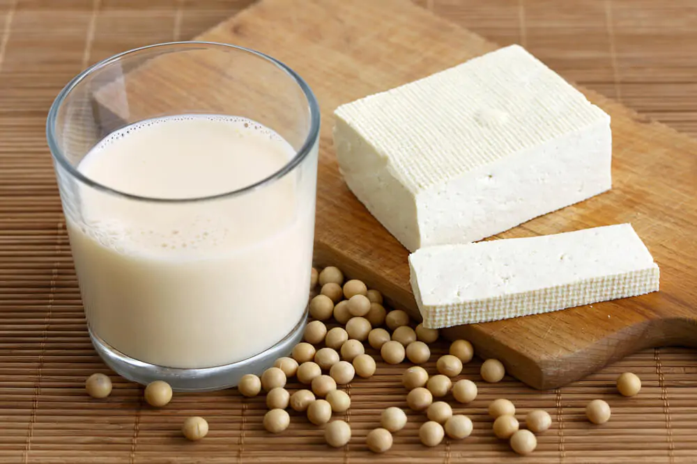Glass of soya milk with froth on bamboo mat with soya beans