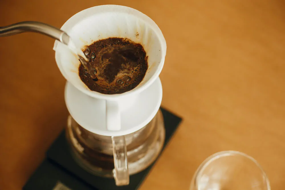 Pouring hot water from steel kettle in filter with ground coffee