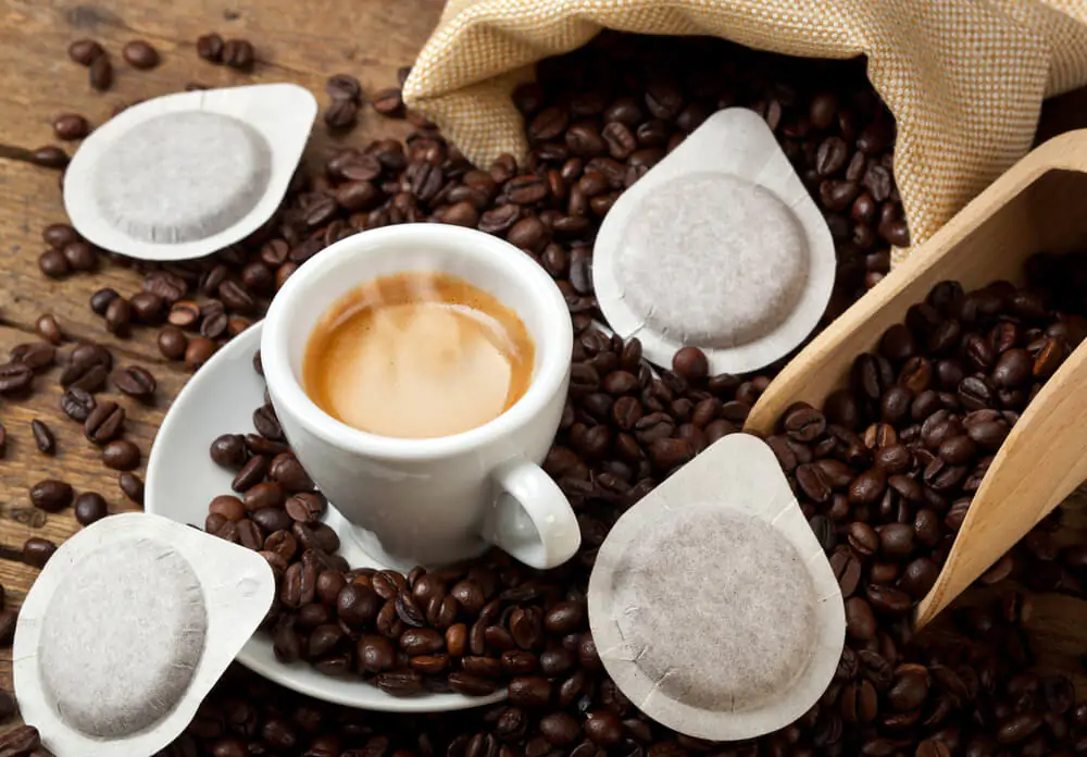 A coffee cup surrounded with coffee beans and coffee pods