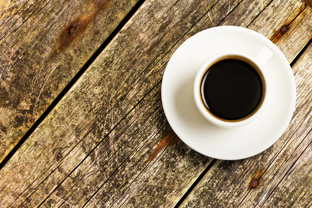 top vie of coffee in a white cup with white saucer placed on a wooden table.
