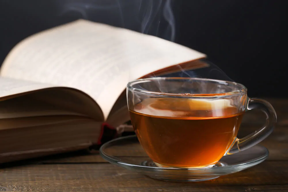 Cup of hot tea with book on table