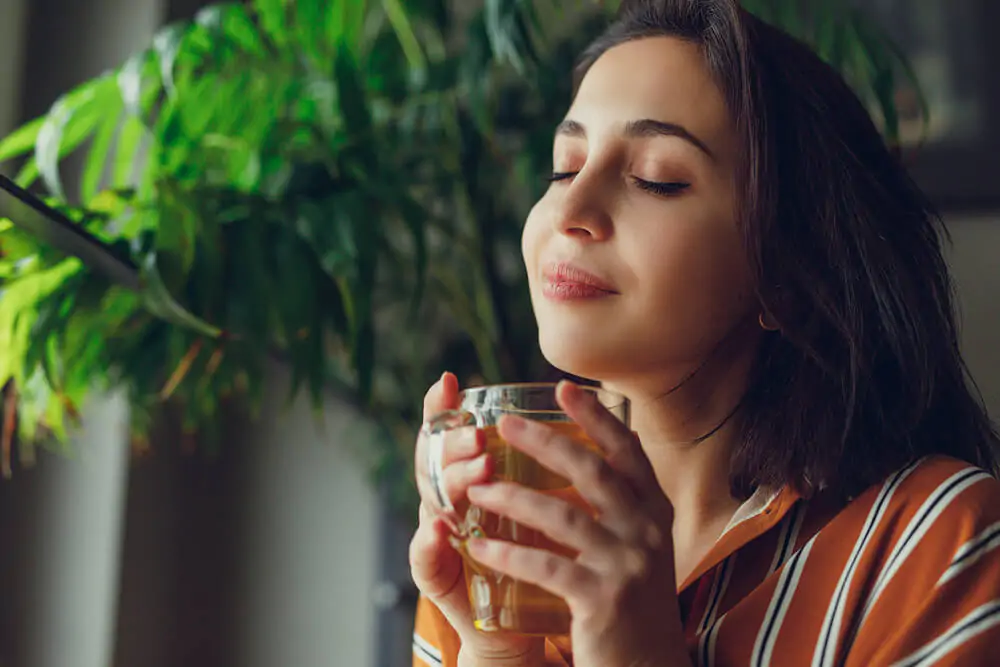 Woman sit on stairs at home, smell her green tea and feels great - what tea is calming