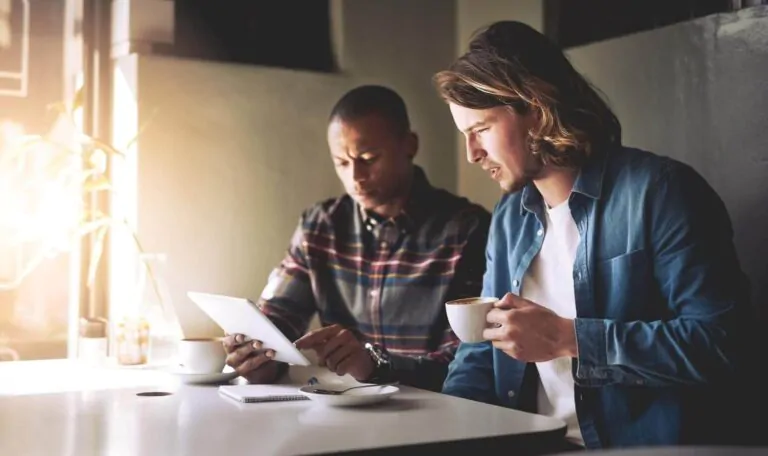 two friends using a tablet while having coffee - best coffee subscription services