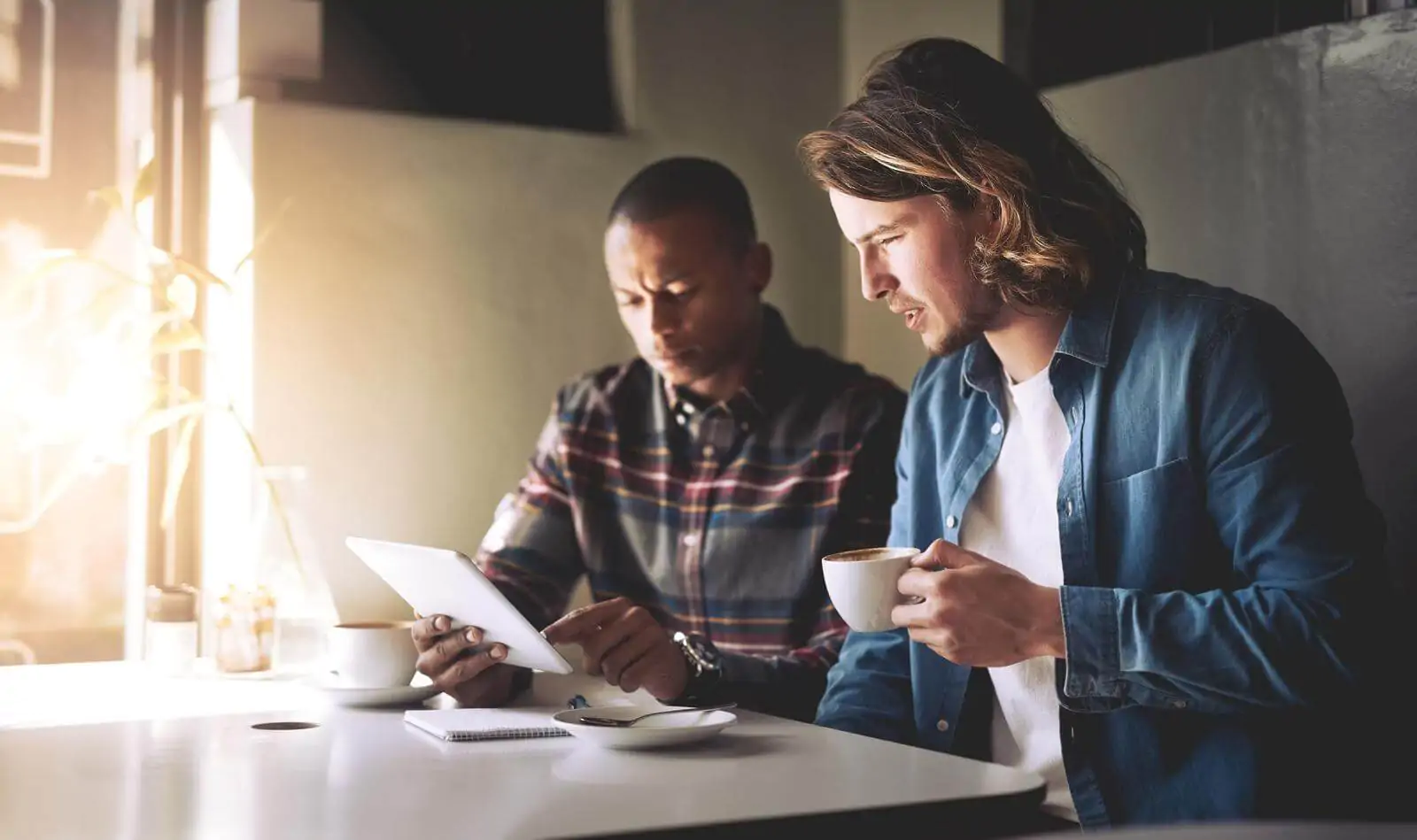 two friends using a tablet while having coffee - best coffee subscription services